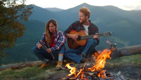 Relaxed-tourists-enjoy-bonfire-spend-evening-in-mountains.-Couple-camp-outdoors.
