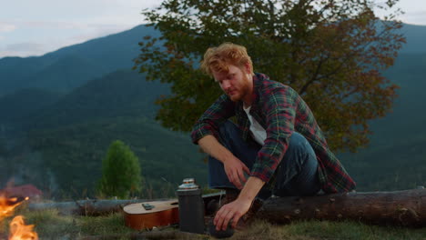 Relaxed-tourist-camping-outside-in-mountains.-Ginger-tourist-warm-hands-by-fire.