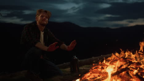 Dreamy-hipster-enjoy-night-fire-burn-on-camp-site.-Closeup-traveler-in-mountains