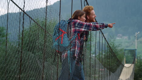 Hikers-look-mountains-view-landscape.-Couple-backpackers-stand-on-river-bridge.