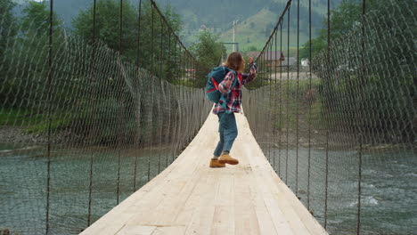 Excited-tourist-hiker-running-on-river-bridge.-Happy-woman-jumping-in-mountains.