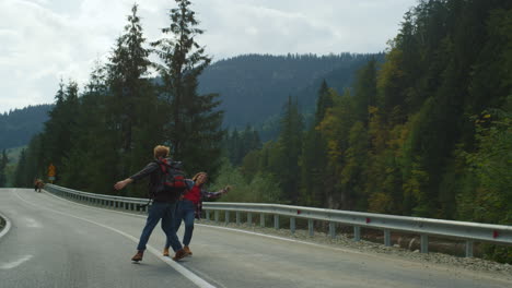 Backpackers-dancing-mountains-road.-Cute-couple-hold-hands-on-nature-travel-trip