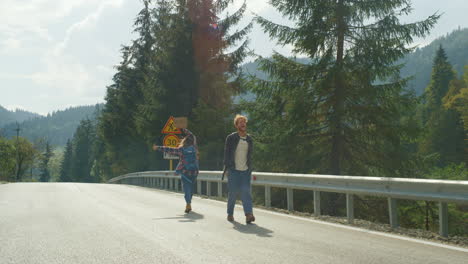 Couple-hikers-stop-car-outside.-Mountain-tourists-move-hands-on-forest-highway.