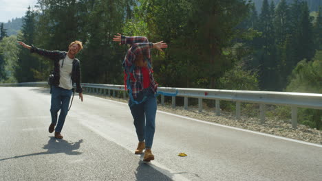 Cheerful-friends-hitchhiking-forest-on-highway-road.-Smiling-couple-enjoy-jump.