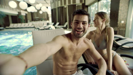 Portrait-of-cheerful-couple-posing-for-selfie-video-near-swimming-pool.