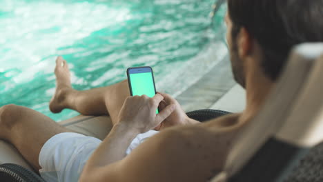 Closeup-young-man-scrolling-mobile-phone-poolside.-Man-hands-holding-smartphone