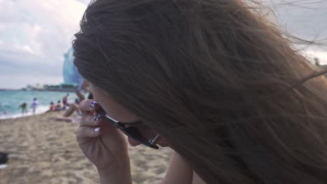 Mädchen-Mit-Sonnenbrille-Und-Am-Strand-Sitzend.-Frau-Mit-Wehendem-Haar-Im-Wind