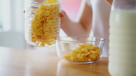 Frauenhände-Gießen-Cornflakes-In-Eine-Glasschüssel.-Nahaufnahme-Der-Müslizubereitung