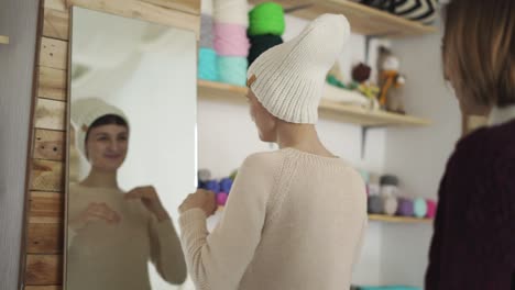 Smiling-woman-dressing-knitted-hat-and-looking-in-mirror-in-show-room