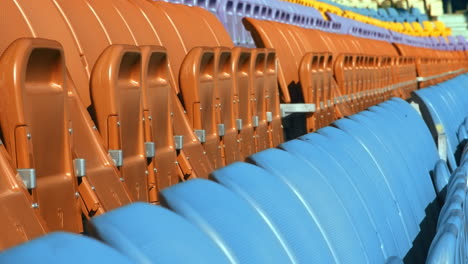 Sitzreihen-Im-Stadion-Mit-Zusammengeklappten-Stühlen.-Nahaufnahme-Leerer-Orangefarbener-Und-Blauer-Sitze