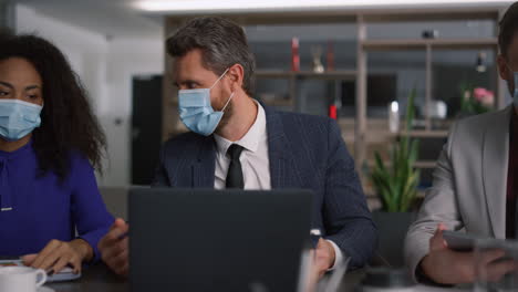 Diverse-business-team-brainstorm-together-wearing-protective-face-mask-in-office