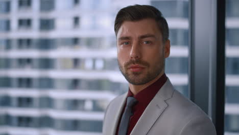 Man-entrepreneur-looking-camera-posing-wearing-formal-suit-in-window-office.