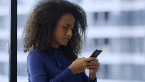Smiling-african-american-businesswoman-texting-mobile-phone-internet-in-office.