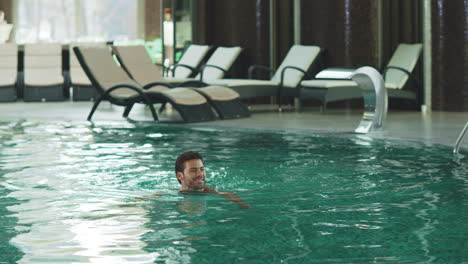 Smiling-man-swimming-at-modern-hotel.-Sexy-guy-bathing-at-luxury-pool-indoor.
