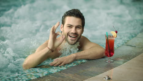 Macro-of-smiling-guy-making-ok-gesture.-Man-posing-for-camera-at-luxury-pool.