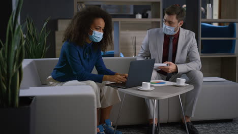 Multinational-business-couple-working-computer-wear-face-masks-at-home-office.