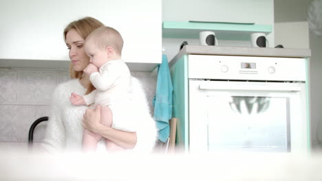 Mother-drinking-coffee-and-hold-little-baby-on-kitchen.-Maternity-leave