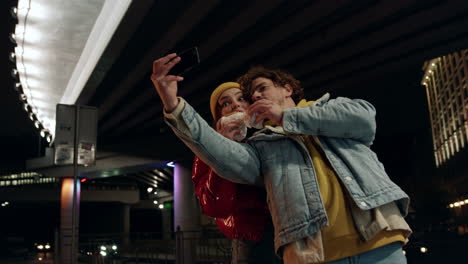 Cheerful-couple-taking-selfie-on-phone-outdoor.-Man-and-woman-eating-burgers.