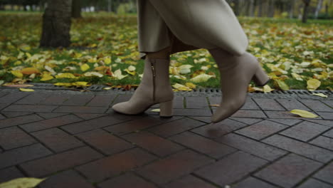 Close-up-woman-legs-in-boots-walking-at-walkway-in-park.-Shoes-going-slowly
