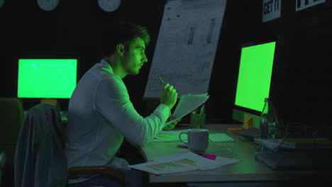 Focused-business-man-working-wih-document-front-green-screen-in-night-office