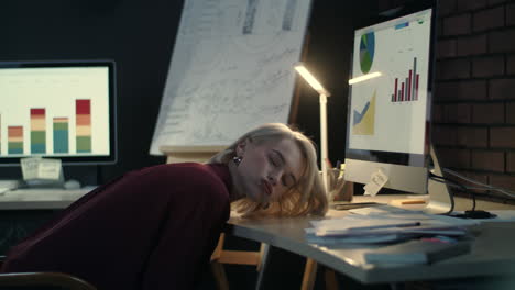 Fatigue-business-woman-lying-on-desktop-in-dark-office.
