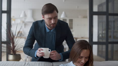 Attractive-husband-bringing-tea-cups-to-wife-at-home.-Woman-talking-with-man.