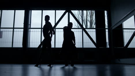 Silhouette-dancers-performing-hip-hop-in-dark-studio.-Guy-and-girl-dancing-.