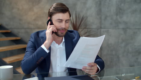 Smiling-businessman-calling-phone-at-workplace.-Happy-man-reading-documents