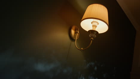 Beautiful-sconce-hanging-on-wall-in-dark-room.-Elegant-lamp-glowing-in-dark.