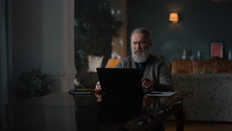 Älterer-Geschäftsmann,-Der-In-Einem-Luxushaus-Einen-Videoanruf-Auf-Einem-Laptop-Führt