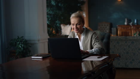 Smiling-old-woman-reading-good-news-on-laptop-computer-at-home