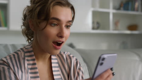 Surprised-woman-using-smartphone-reading-messages-in-pajamas-at-home-closeup.