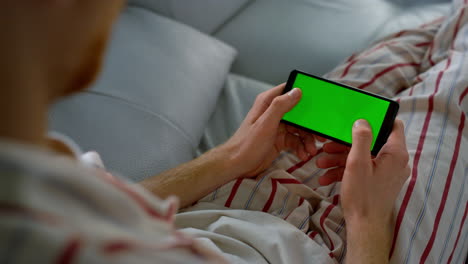 Man-typing-green-screen-on-smartphone-at-home.-Player-enjoy-online-game-closeup