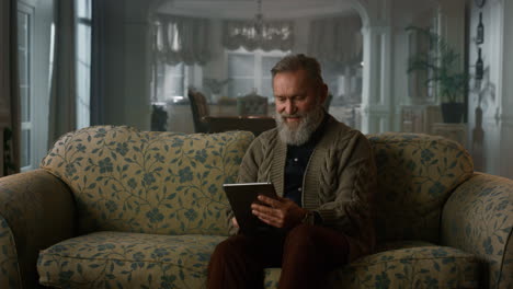 Ruhiger-älterer-Mann,-Der-Einen-Tablet-Computer-Auf-Dem-Sofa-Benutzt.-Pensionierter-Großvaterblock