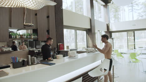 Young-man-moving-to-bar-at-wellness-resort.-Guy-taking-bottle-water-bar-counter.
