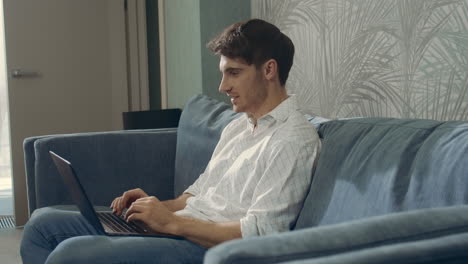 Laughing-man-reading-message-computer.-Happy-guy-sitting-couch-with-laptop.