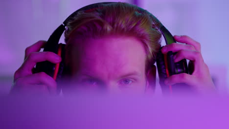 Neon-guy-playing-games-on-computer-closeup.-Focused-student-wearing-headphones