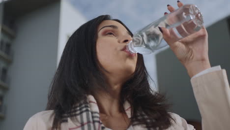 Businesswoman-drinking-water-from-bottle-on-street.-Girl-enjoying-fresh-water