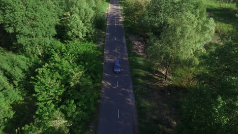 Car-moving-on-countryside-road-through-summer-forest-aerial-view