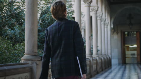 Student-reading-notes-in-workbook-at-university.-Businessman-walking-in-hallway