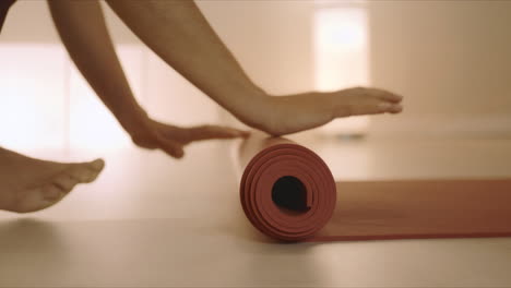 Frauenhände-Rollen-Yogamatte-Nach-Dem-Training-Zusammen.-Mädchen-Faltet-Fitnessmatte-Auf-Dem-Boden