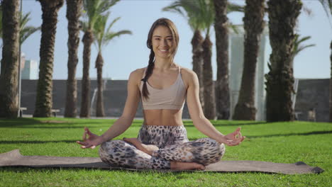 Entrenador-De-Yoga-Sonriente-Sentado-En-Una-Alfombra-En-El-Parque.-Niña-Posando-Ante-La-Cámara-Al-Aire-Libre