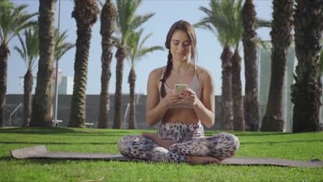 Woman-sitting-in-lotus-pose-with-smartphone.-Girl-using-cellphone-in-park