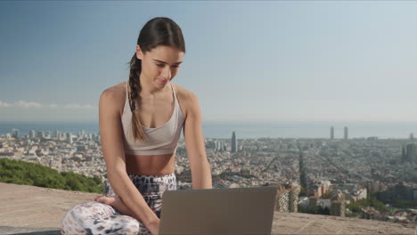 Woman-sitting-in-lotus-pose-with-laptop-outdoors.-Girl-typing-on-laptop-in-city