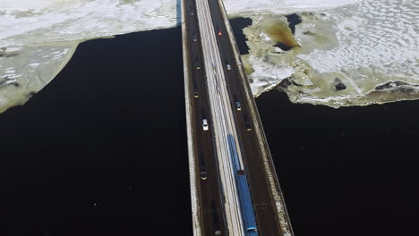 Aerial-view-car-motion-on-highway-bridge-over-frozen-river-in-winter-city