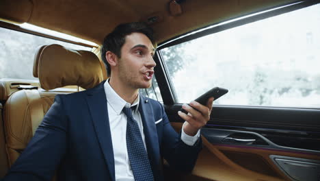Smiling-business-man-dictating-message-on-smartphone-in-salon-of-business-car.