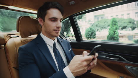 Portrait-of-smiling-businessman-typing-message-on-smartphone-in-business-car.