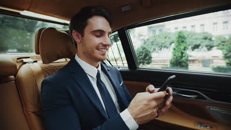 Fröhlicher-Geschäftsmann,-Der-Im-Luxusauto-Eine-Nachricht-Auf-Dem-Smartphone-Schreibt.