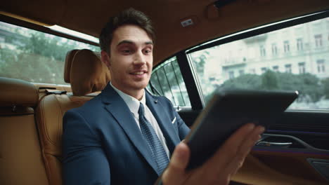 Happy-male-professional-reading-messages-on-tablet-computer-in-business-car.