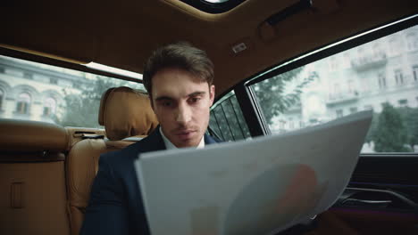Portrait-of-focused-business-man-reading-documents-on-back-seat-of-automobile.